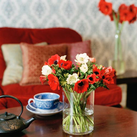 Julbukett med röda och vita snittblommor â amaryllis, rosor, liljor, ranunkel och hyacint â omgiven av eukalyptus, jĂ€rnek och murgröna, dekorerad med kvistar, kanel och stjĂ€rnanis.
