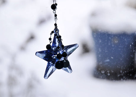 Vit juldekoration med blå stjärna i december; symbol för vintersolstånd och ljusare tider, advent och Lucia, med vita vinterblommor (amaryllis, hyacinter, julros), ljusslingor, islyktor och vintergröna växter i trädgården inför jul och nyår.