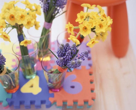Busiga blommor – vårens trendiga påskbukett med gula narcisser (påskliljor), tulpaner, pärlhyacinter, ranunkler, anemoner och videkissar i rundad keramisk vas i gult, grönt, lila och himmelsblått.