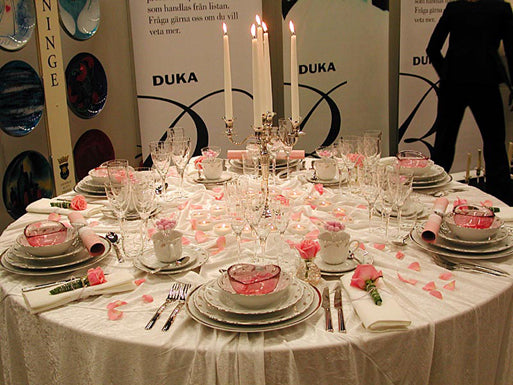 Temafest – rosor: Dukas romantiska rosavita dukning med små rosa rosor på servetter och i glas, rosenblad på krossad velourduk, silverkandelabrar, nysilverbestick, vita silverkantade tallrikar och rosa glasskålar.