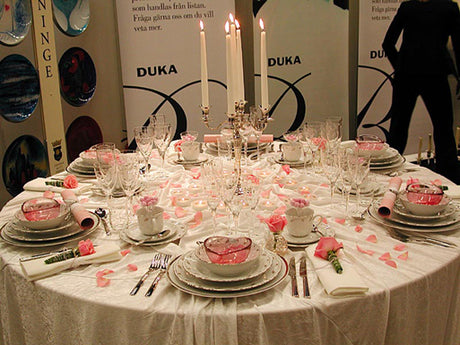 Temafest – rosor: Dukas romantiska rosavita dukning med små rosa rosor på servetter och i glas, rosenblad på krossad velourduk, silverkandelabrar, nysilverbestick, vita silverkantade tallrikar och rosa glasskålar.