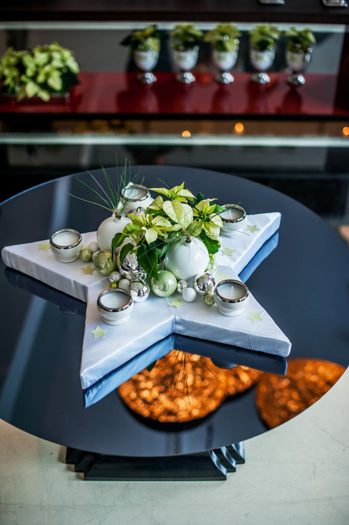 Elegant arrangemang med gräddvita och milt gröna julstjärnor i silvriga och vita krukor, kombinerat med gröna och silvriga julgranskulor och höga vita ljus, inspirerat av Breakfast at Tiffany’s; perfekt som stilrent julbord under advent och nyår.