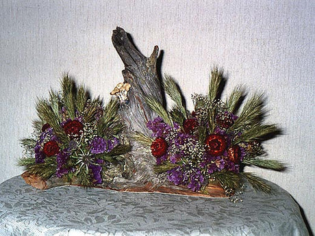 Arrangemang av torkade blommor på en grånad träbit – naturligt kärl av trä med gräs, fröställningar, kvistar och mossa; hållbar inredning med naturmaterial, återbruk och DIY-inspiration för att plocka, torka och arrangera blommor.