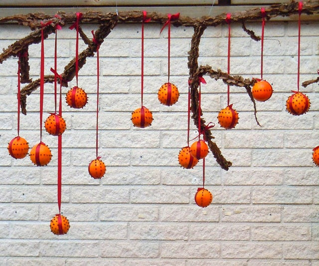Modern pomander med apelsiner och hela kryddnejlikor, bundna med julrött sidenband på gren – juldoftande dekoration och naturlig luftfräschare, perfekt som centerpiece.